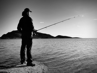 Fisherman check fishing line and pushing bait on the rod, prepare himself and throw lure far into peaceful water.