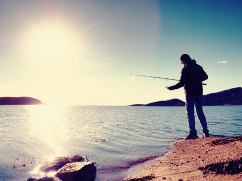 Fisherman check fishing line and pushing bait on the rod, prepare himself and throw lure far into peaceful water.