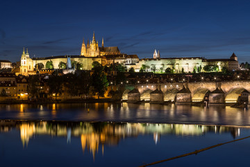 Fototapeta na wymiar View of the lit Prague (Hradcany) Castle, Charles Bridge (Karluv most) and their reflections on the Vltava River in Prague, Czech Republic, in the evening.