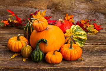 pile of raw orange and green pumpkins with fall leaves on wooden table