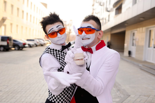 Two mimes in dental glasses are holding a cast of the jaw in their hands. Dental prosthetics