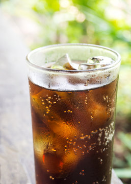 Black soft drink in glass. Garden view with bokeh. Favorite soft drink for refreshment.