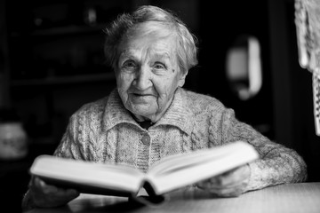 Elderly woman sitting at a table reading a book. Black-and-white contrast portrait.