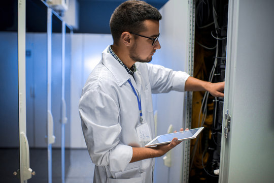 Side view portrait of young scientist looking in server cabinet while working with supercomputer in data center