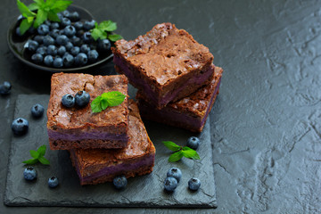 Chocolate brownies with blueberries and cream filling. Dark background.