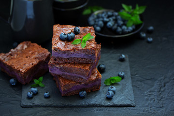 Chocolate brownies with blueberries and cream filling. Dark background.