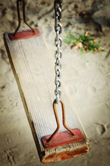 Old wooden swing on an iron chain.