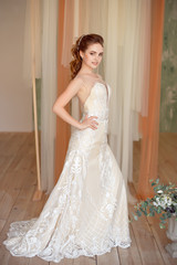 Full-length portrait of Beautiful luxurious female model with medium brown hair in a long white wedding dress in the room. Bridal clothes concept. Stylish wedding dress.