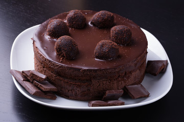 Homemade chocolate biscuit cake and dark chocolate segments on a white plate
