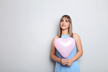 Portrait of young woman with pink heart balloon on grey background
