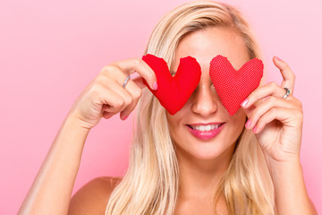  Happy young woman holding heart cushions on a pink background