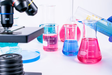 hand of scientist pouring into flask colorful liquid. examining samples in laboratory and close up of microscope . laboratory science, clinic and research concept. 