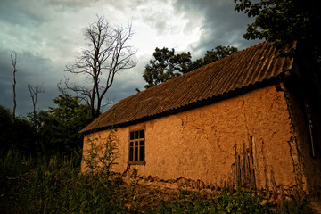 Fototapeta na wymiar Old Ukrainian village house (mud hut) at sunset on the edge of the forest