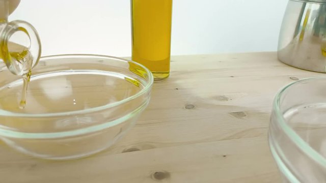 pouring cooking olive oil in the bottle in the white container on wood table background near olive oil bottle, shot in slow motion on white background, concept of healthy food diet and nutrition