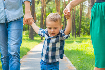 Fototapeta na wymiar Dad and mom raised their son upside and walking along the park path