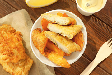 Plastic plate with tasty fried fish and potatoes on table