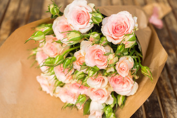 Bouquet of pale pink blooming fresh roses with buds n wrap on wooden table