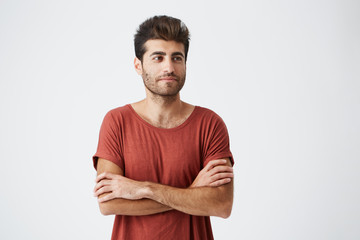 Young spanish hipster wearing red tshirt slightly smiling , keeping hands crossed, and meditative looking aside during magazine photoshoot. Beauty, people, youth and lifestyle concept