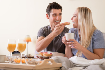 Happy young couple eating bread and strawberry jam while having breakfast in bed