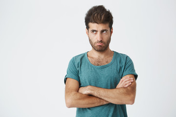 Close up isolated portrait of unhappy hispanic guy in trendy clothes and haircut, looking away, pursuing lips expressing insult and dissatisfaction. Human emotions. Copy space.