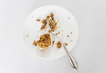 Carrot cake leftovers with fork on a dessert plate on a light background
