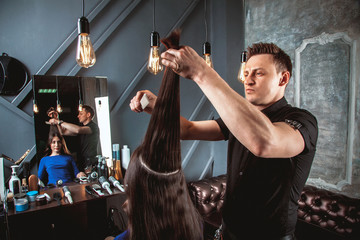 Hairdresser cutting hair, does a hairstyle of girl client. Hairstylist serving client at barber shop.