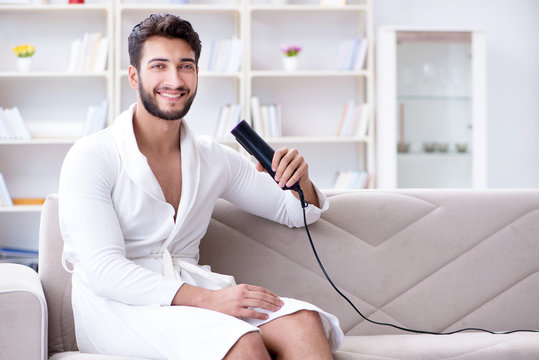 Young man drying hair at home with a hair dryer blower 