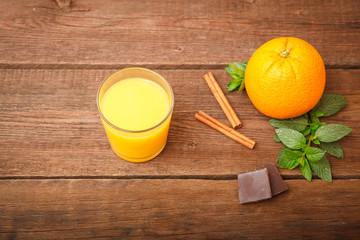 Freshly squeezed orange juice in a glass on a wooden background. Orange, melissa, cinnamon and...