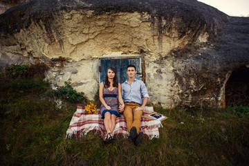 Fototapeta na wymiar Sensual lovely couple sitting on the plaid near the rock with caves and blue wooden door.