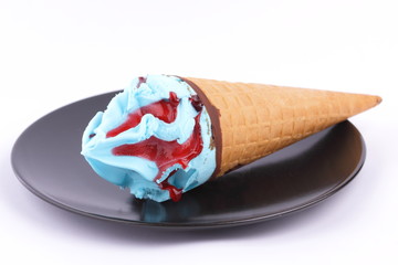 Ice cream in a waffle cup with a multicolored filling and red jam on a black plate with a wooden spoon for the designer