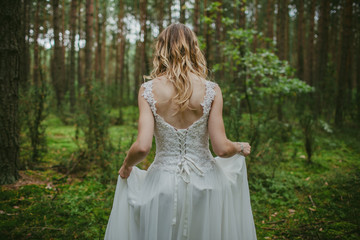 Bride in white wedding dress walking in forest. Fashion and nature background.