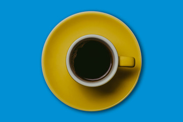 Yellow small espresso cup with coffee inside isolated on blue.