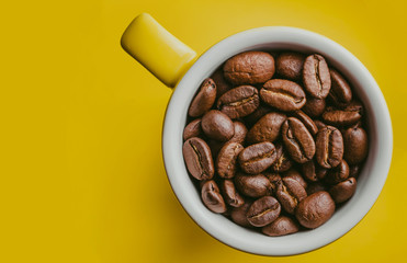 Yellow small espresso cup with coffee seeds inside isolated on yellow background.