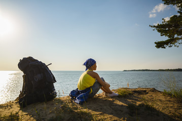 Boy sitting on sand cliff looking to sea. Travel and tourism concept