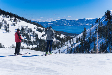 Two middle aged men on skis look out over the lake tahoe mountains