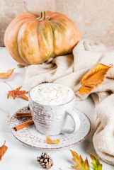 Autumn hot drinks. Pumpkin latte with whipped cream, cinnamon and anise on a white marble table, with a sweater (blanket), autumn leaves and fir cones. Copy space