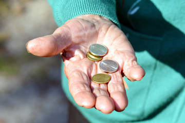 The coins are in the hands of the old lady. An elderly woman with money in her hands. Poverty alms