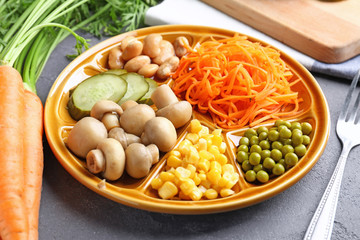 Plate with delicious carrot salad and different vegetables on table