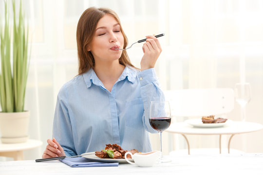 Young woman eating delicious ribs in restaurant