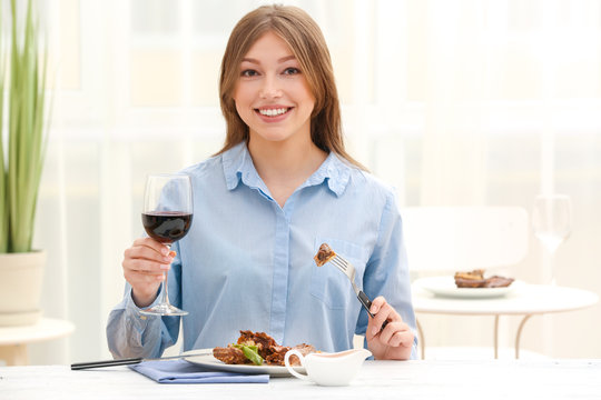 Young woman eating delicious ribs in restaurant