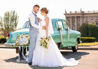 Happy wedding couple near decorated car outdoors