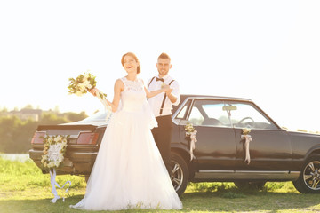 Happy wedding couple near decorated car outdoors