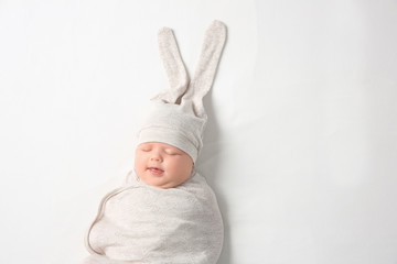 Cute newborn baby in cocoon and funny hat on white background