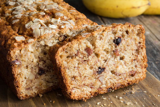 Sliced banana bread loaf with walnuts and oats on wooden cutting board. Closeup view, horizontal