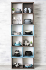 Storage stand with ceramic dishware on light wall background