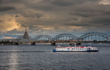 Fototapeta premium Sightseeing cruise boat on the river Daugava in Latvian capital Riga. Railway bridge in the background.
