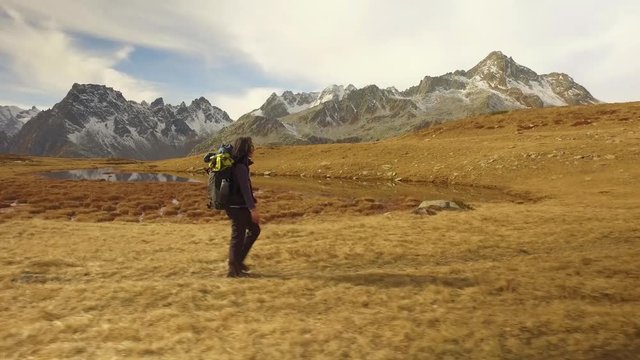 woman hiker walking on fall fields near lake path to snowy mounts.Following side view. Sunny autumn day Hiking in colorful red forest wild nature mountain outdoors.Alps Devero lake park. 4k video
