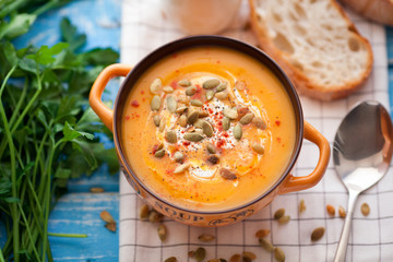 Homemade pumpkin soup with cream, bread, greens and pumpkin seeds on a wooden background. Top view