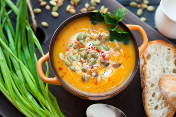 Homemade pumpkin soup with cream, bread, greens and pumpkin seeds on a wooden background. Top viev