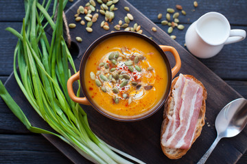 Homemade pumpkin soup with cream, bread, bacon and pumpkin seeds on a wooden background. Top viev